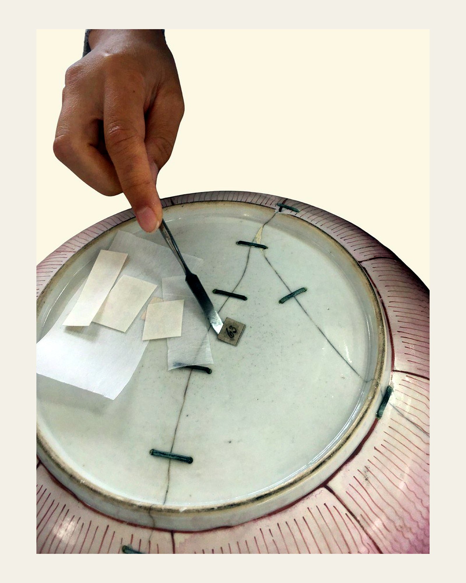 Museum labels being removed from the porcelain dish for preservation.