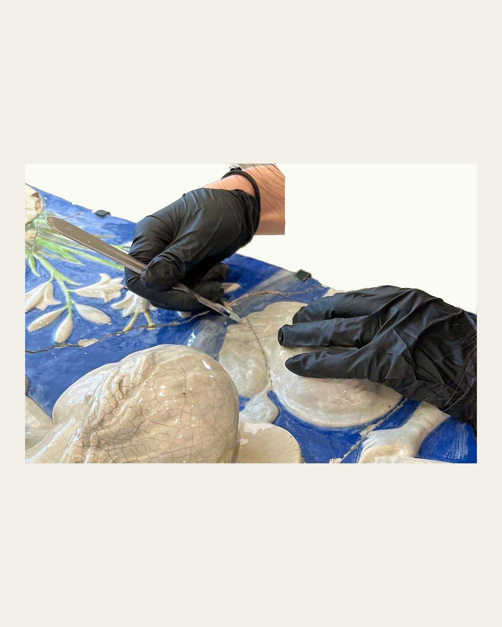 Gloved hands mechanically removing failing plaster fills from the plaque.