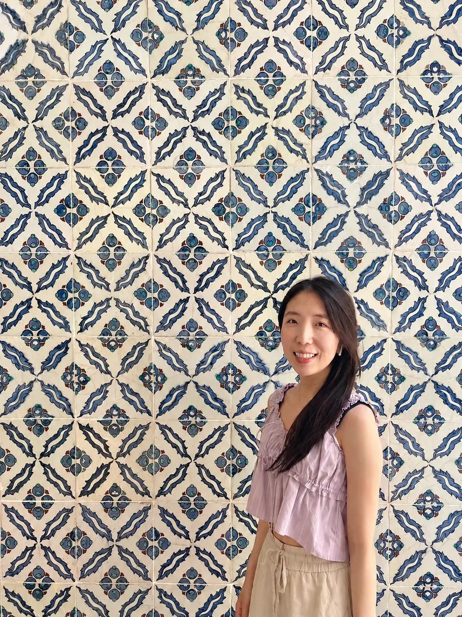 Sujin Jung standing in front of a blue-and-white decorative tile wall.